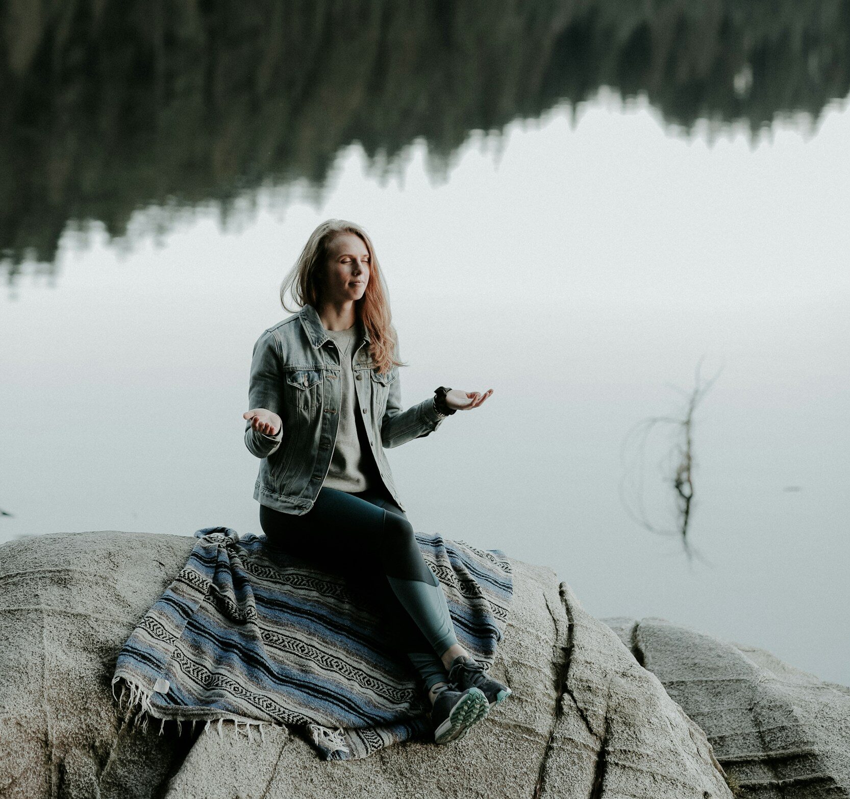 woman meditating on rock in bank of lake